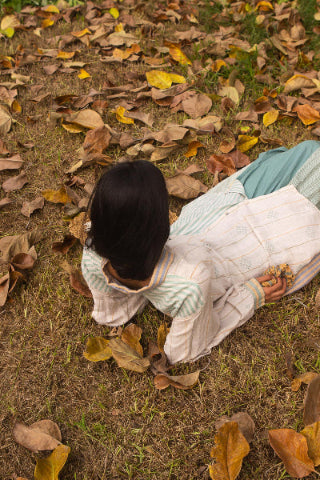 women laying down on the ground surrounded by autumn leaves wearing linen shirt